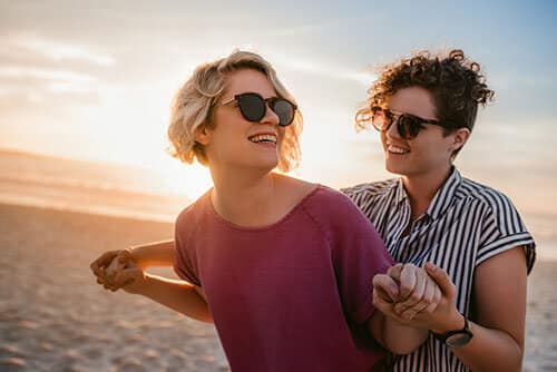 Two women holding hands and posing for photo on the beach.