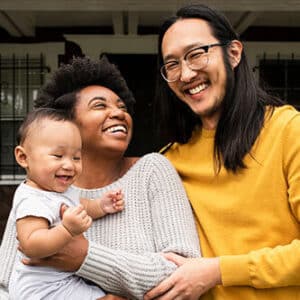 Interracial couple with baby standing on front porch of home.