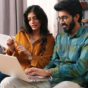 Indian man and woman sitting together on couch reading off credit card and using laptop.