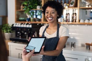 Female barista holding out tablet to customer to scan for payment.