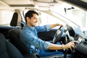 Man sitting in driver's seat of car with one hand on the steering wheel and the other using dashboard screen.