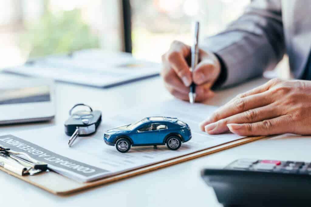 Person sitting at desk signing for a an auto loan with toy car, key, and calculator sitting in front of them.