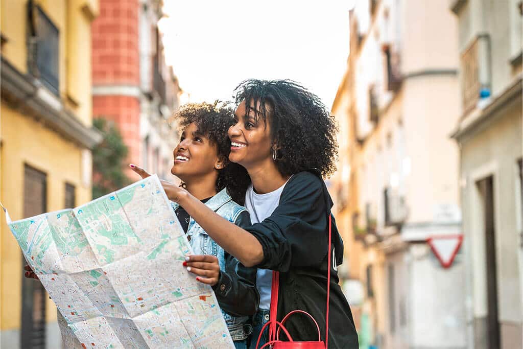 Mother and daughter holding map in city while looking up at building.