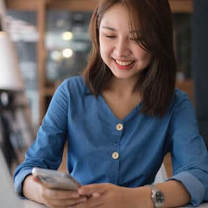 Woman sitting at a table smiling holding phone in her hands.