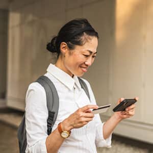 Woman standing outside holding credit card and looking at cell phone.